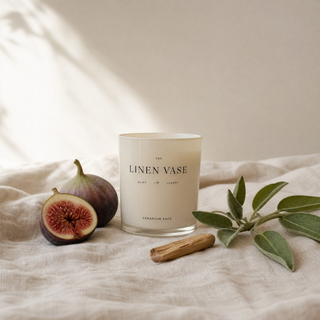 Geranium Sage Signature Candle on a white linen tablecloth with fresh figs and sage