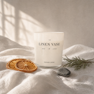 Vetiver Cedar Signature Candle on a white linen tablecloth with dried orange slices and cedar