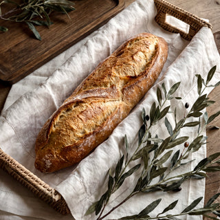 Willa Rattan Narrow Display Tray lined with a pure linen napkin holding fresh bread with faux olive stems